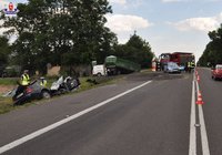 fot. miejsce wypadku drogowego, rozbity volkswagen, w tle przyczepa i ciągnik rolniczy, policjanci, strażacy, ratownicy oraz wóz strażacki