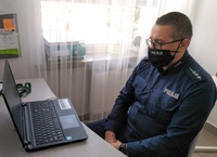 policjant w maseczce przed laptopem w czasie zajęć profilaktycznych z uczniami