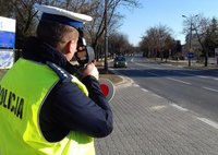 stojący na poboczu drogi policjant z ruchu drogowego w czasie mierzenia prędkości