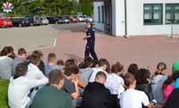 policjant w czasie spotkania z uczniami ze szkoły podstawowej w Miączynie, młodzież siedzi na trawie