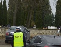 odwrócony tyłem policjant z ruchu drogowego stojący przed murem cmentarza