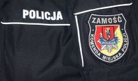 napis policja na policyjnej kurtce oraz na rękawie naszywka - logo Komendy Miejskiej Policji w Zamościu